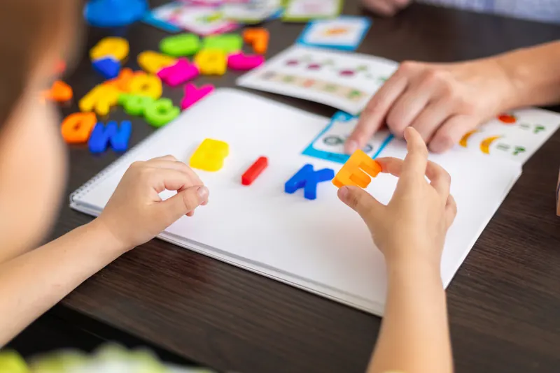 Lerntherapie: Ein Kind legt gemeinsam mit einer Therapeutin Wörter aus bunten Buchstaben